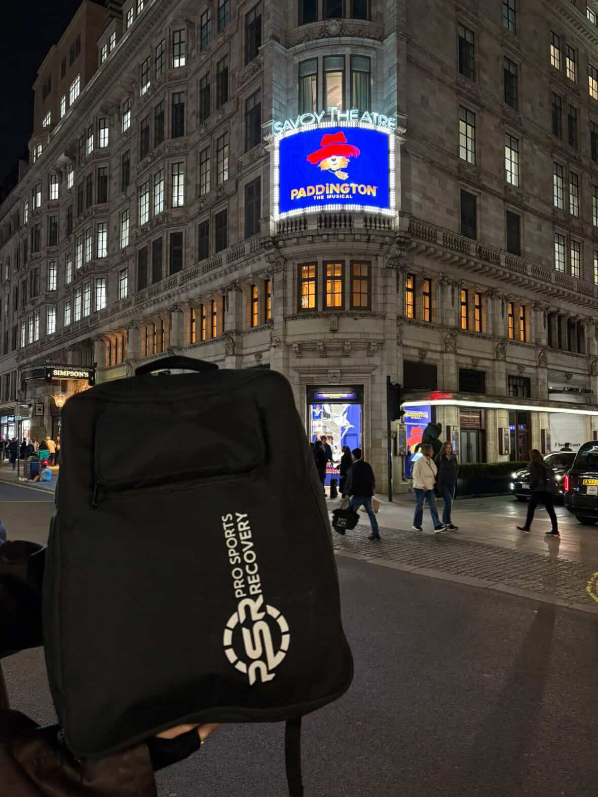Pro Sports Recovery backpack held up outside the Savoy Theatre under the Paddington the Musical sign
